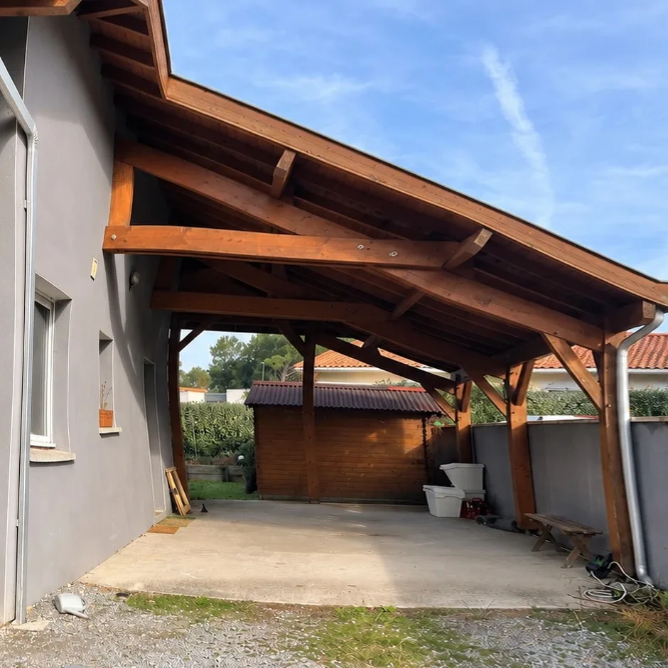 L'auvent avant travaux, charpente bois ouverte sur poteaux, dalle béton nue et abri de jardin au fond.