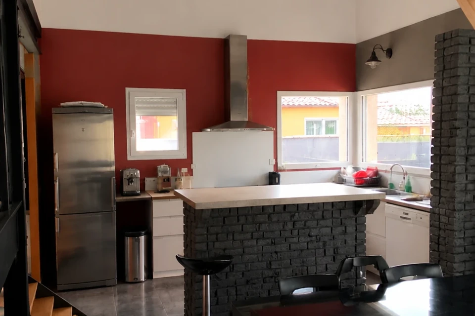 Cuisine avant travaux, mur rouge, réfrigérateur inox et bar en briques noires.