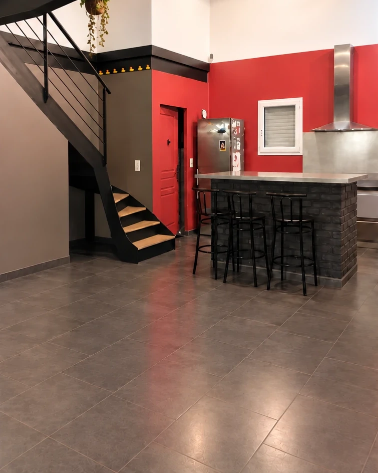 La même pièce avant travaux, murs rouge et taupe, bar en briques noires et tabourets métalliques.