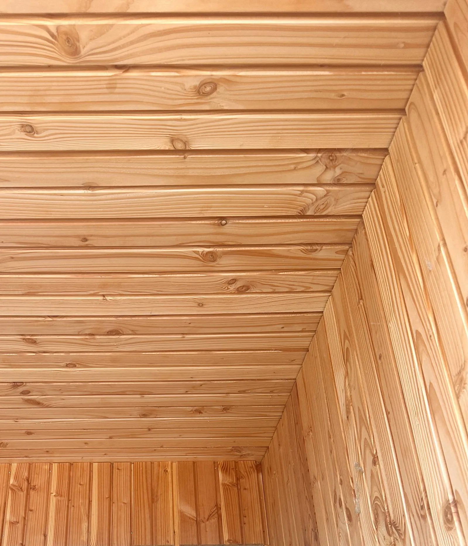 Détail de l'entrée en retrait, bardage bois clair à lames verticales sur les parois et à lames horizontales au plafond, qui se rejoignent dans l'angle.