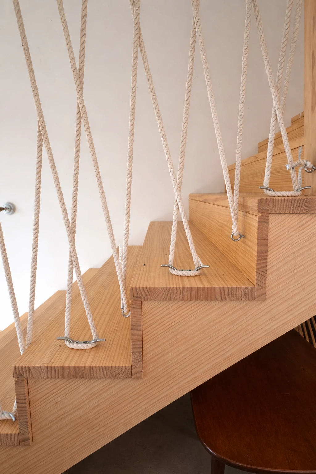 Gros plan sur les marches en bois de l'escalier, des cordages blancs croisés fixés aux marches par des taquets métalliques de bateau.